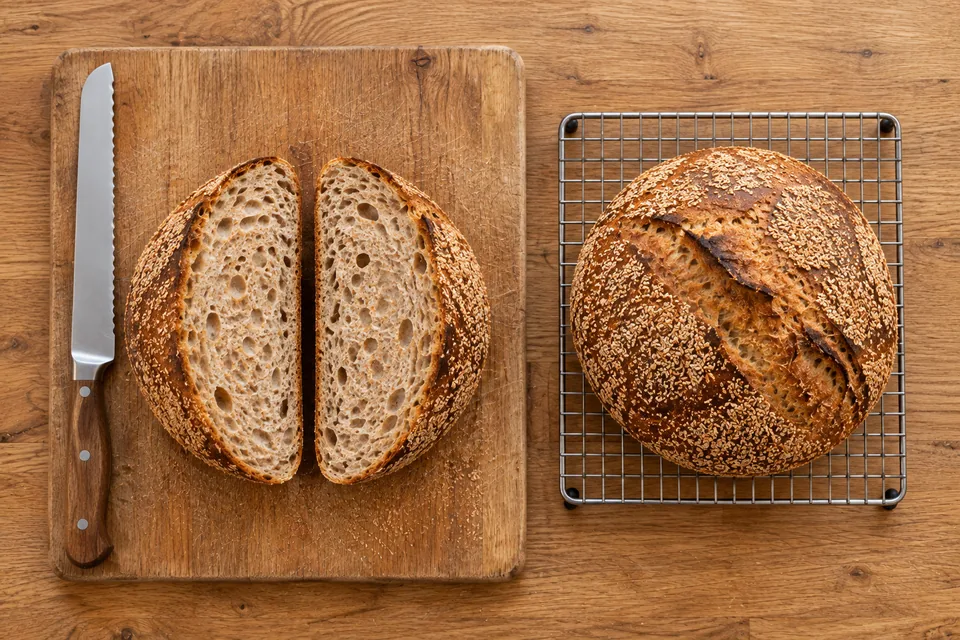 Overhead view of two matching cut halves on a board and the second whole bran-coated round on a rack.