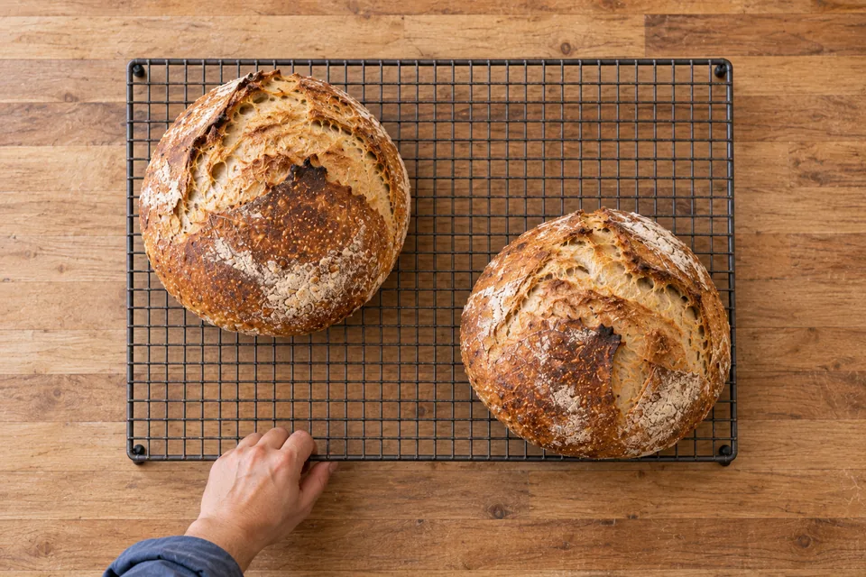 Two intact round white loaves arranged diagonally on a cooling rack, viewed from above.