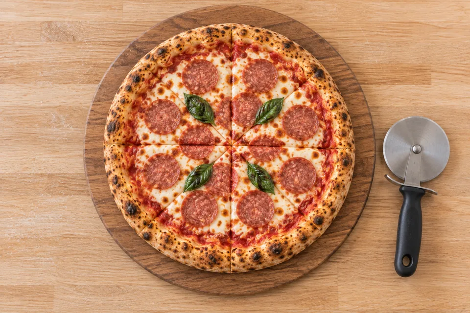 An overhead view of a beef salami pizza cut into eight wedges on a round wooden board.