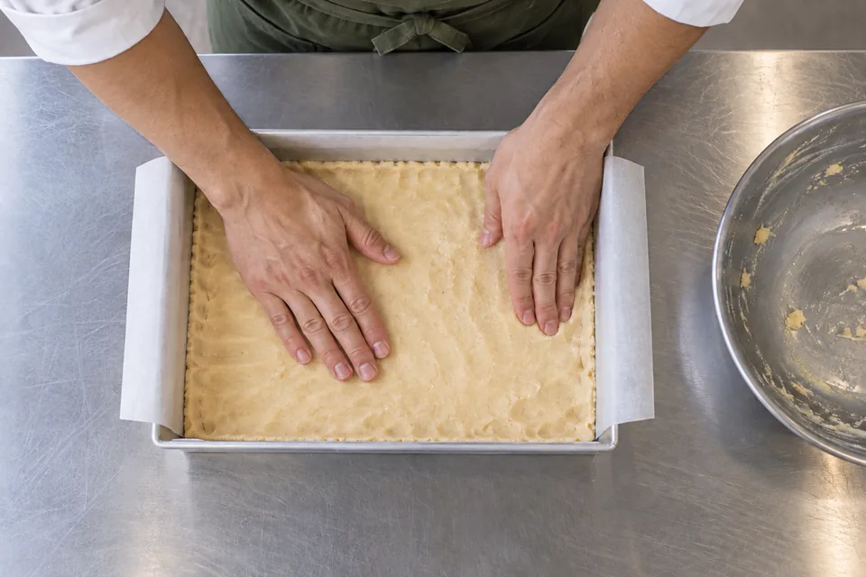 Overhead view of shortbread dough being pressed into a tin.