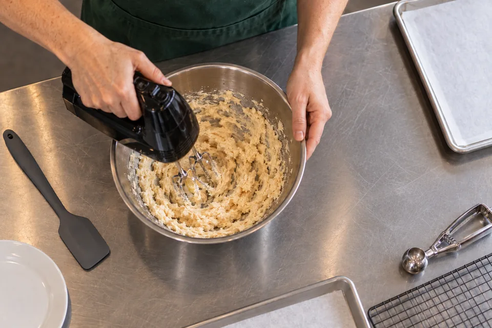 Overhead view of a hand mixer beating pale butter and sugar.